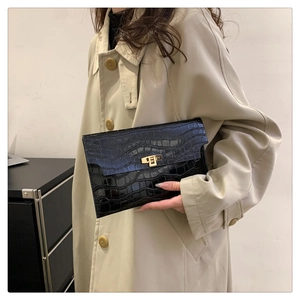 Detail of black crocodile texture clutch bag with golden clasp held by a woman in beige coat