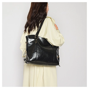 Detail of black wax leather tote bag with gold ring hardware worn with a beige trench coat