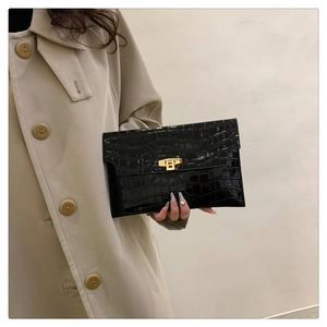 Detail view of a black patent leather clutch with crocodile pattern and golden turn lock