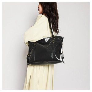 Detail of minimalist black glossy tote bag with gold metal buckle on female shoulder