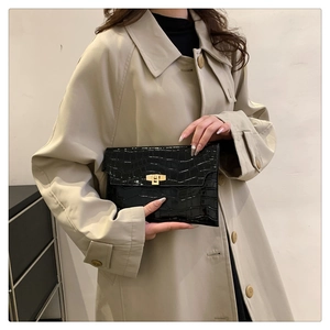 Detail of black crocodile texture clutch bag with gold buckle on beige trench coat