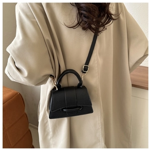 Detail of black litchi texture leather mini bag with gold hardware and shoulder strap
