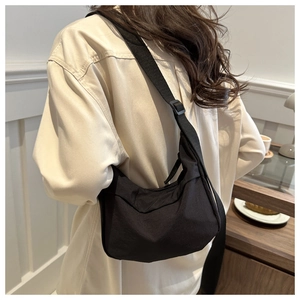 Side view of a black crescent crossbody bag worn by a model in a minimalist room