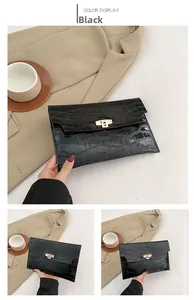 Detail of black glossy crocodile pattern envelope clutch bag with gold buckle fastener