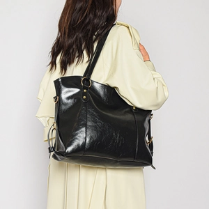 Minimalist black glossy underarm tote bag with gold metal buckle shown on shoulder