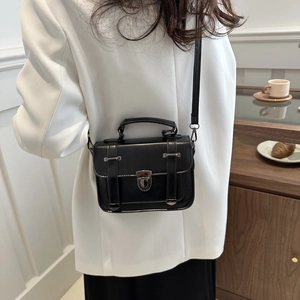 Petit sac carré vintage noir avec boucles porté sur un blazer blanc classique