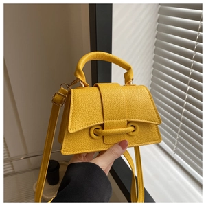 Close-up of yellow leathery mini tote bag with golden buckle and textured finish