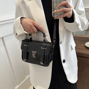 Sac bandoulière noir chic avec boucle argentée porté sur une veste de tailleur blanc