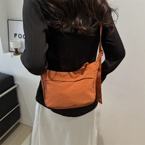 Minimalist orange nylon crescent tote bag shown on model in a modern lifestyle setting
