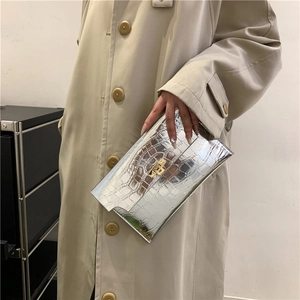 Silver envelope clutch bag with crocodile pattern and golden clasp held by a model