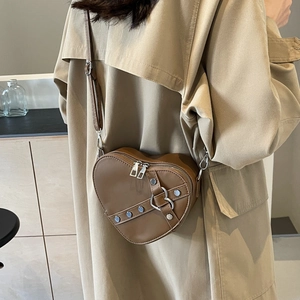 Sac bandoulière marron en forme de cœur avec clous argentés porté par un mannequin