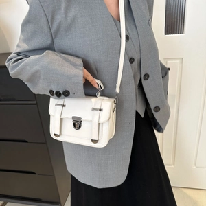 Petit sac carré blanc avec boucles décoratives porté sur un blazer gris chic