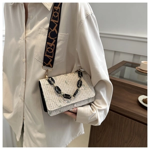 Close-up of beige woven crossbody bag with green floral embroidery and chunky gold chain