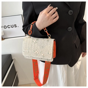 Detail of a woven flap bag with floral embroidery and vibrant orange acrylic chain strap