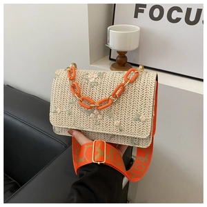 Détail d'un sac tissé beige avec broderie florale et poignée en chaîne orange vif