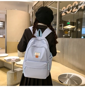 Detailed back view of a light blue nylon school backpack featuring functional side buckles