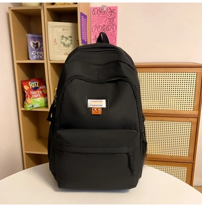 Detailed close-up of a black nylon backpack featuring fashion labels and a smile charm