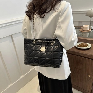 Élégant sac cabas noir matelassé avec bandoulière chaîne et fermoir porté à l'épaule