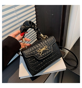 Detail of black quilted shoulder bag featuring gold bow and pleated cloud handle