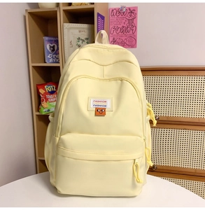Detailed view of cream nylon backpack featuring front zipper pocket and fashion patch