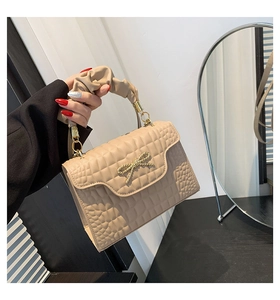 Close-up of quilted beige handbag with golden bow buckle and trendy scrunchie handle