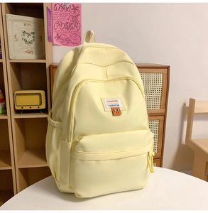 Detail view of the yellow nylon backpack with multi-pocket design and smiling charm
