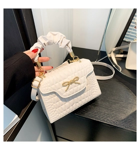 Close-up of white quilted handbag featuring a gold bow buckle and pleated cloud handle