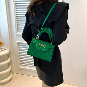 Green faux-crocodile leather flap bag with gold bow and gathered handle on a black dress