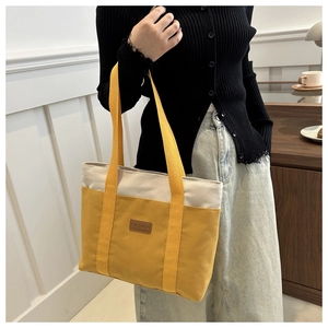 Detail of yellow and beige canvas tote bag with FASHION leather patch and woven handles