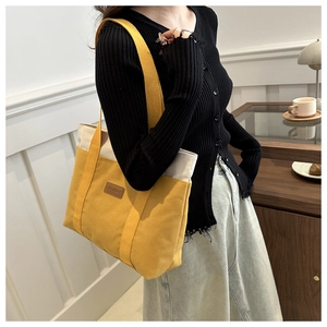 Detail of yellow canvas tote bag with contrast cream trim and brown leather fashion tag
