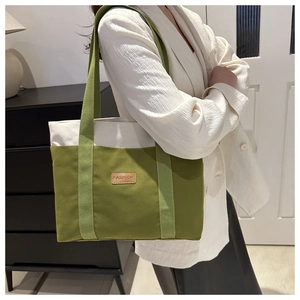 Detail of green and beige canvas tote bag with a brown leather FASHION label and wide strap
