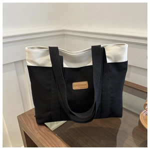 Close-up of contrast canvas tote bag featuring brown leather fashion logo and black strap