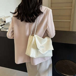 Chic beige patent leather tote bag with silver chain strap shown on a model