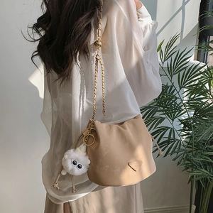 Minimalist apricot drawstring bucket bag with gold chain strap and plush ball charm