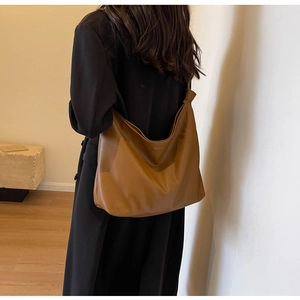 Detail of a brown leather tote bag with a unique knot shoulder strap on a black wool coat