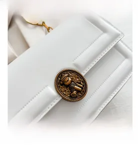 Detail of white leather bag with antique bronze bear embossed metal buckle and top stitching