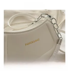 Detail of white PU leather crescent bag with silver chain strap and gold logo text