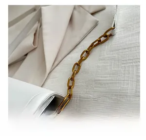 Detail of white leather shoulder bag featuring gold chain link and precise stitching