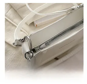 Close-up of smooth silver zipper and FASHION & BAGS engraving on white leather shoulder bag