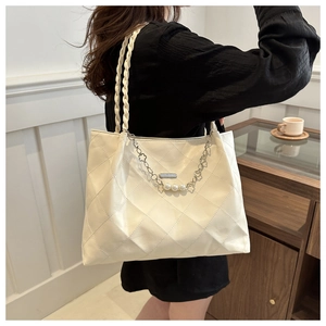 Close-up of beige quilted tote bag with woven handles and pearl flower charm detail