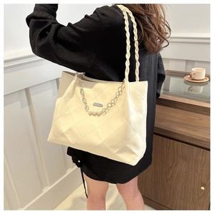 Detail of cream quilted tote bag featuring woven leather strap and pearl floral chain