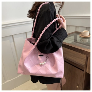 Detail of pink quilted tote bag with pearl charms and woven shoulder strap on a model