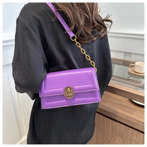 Detail view of purple leather crossbody bag with vintage gold emblem and chain strap