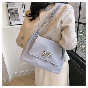 Close-up of a light blue suede butterfly bag with a metal chain strap on a female model