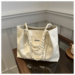 Detail of quilted tote bag with pearl-accented woven handles and elegant metal plaque