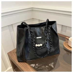 Detail of black quilted tote bag featuring woven handles and pearl chain accent
