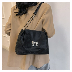 Detail of black matte crossbody bag with silver butterfly buckle and chain strap on a model
