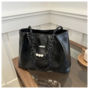 Detail of black quilted tote bag with braided handle and elegant pearl chain ornament