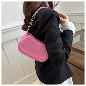 Pink leather shoulder bag with chain handle shown on model in a minimalist setting