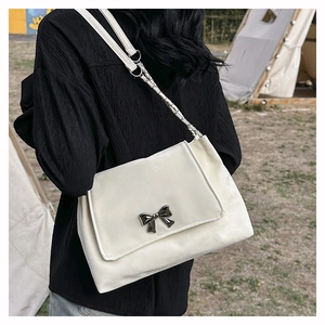Detail of off-white faux leather shoulder bag with silver butterfly buckle in outdoor setting
